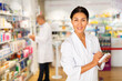 © JackF - Asian female pharmacist in lab coat standing in salesroom of drugstore and writing recipe in blank.
