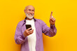 © Богдан Маліцький - old bald grandfather with gray beard uses smartphone and points with his finger on yellow isolated background