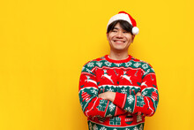 Young Asian Man In Christmas Sweater And Santa Hat Standing With Crossed Arms Over Yellow Isolated Background