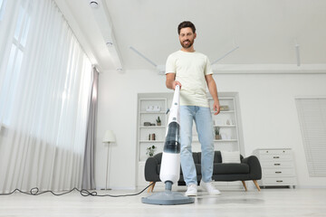 Wall Mural - Happy man cleaning floor with steam mop at home, low angle view