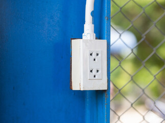 White electrical outlet plug mounted on a blue metal wall.