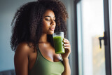 Young attractive african american woman drinking her detox juice after workout, beautiful athletic female drinking green juice at home