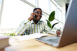 © fotofabrika - African man entrepreneur talking on cellphone and working on laptop at office