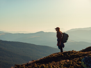 Wall Mural - Silhouette of hiker woman with backpack relaxing on top of a mountain and enjoying the valley view. Concept of tourism and travel