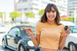 © luismolinero - Young woman holding car keys at outdoors surprised and pointing finger to the side