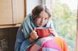 © Westend61 - Sick girl wrapped in blanket and sitting with coffee cup at home