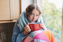 Sick Girl Wrapped In Blanket And Sitting With Coffee Cup At Home
