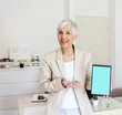 © Jelena Stanojkovic - Portrait of a mature businesswoman holding up a digital tablet with a blank screen in an home office.