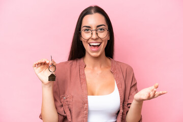 Poster - Young woman holding home keys isolated on pink background with shocked facial expression