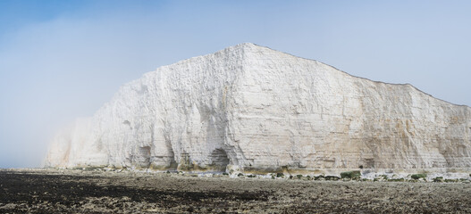 Wall Mural - Misty morning in Hope Gap beach, Cuckmere Haven, located between Seaford and Eastbourne. Panorama. Pebbly coastline with seaweed and the white cliffs on the background, selective focus