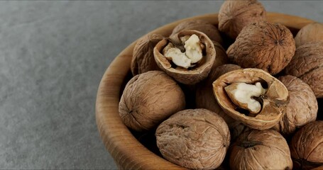 Wall Mural - Wooden bowl with walnuts on a gray background. Close-up footage on the rotating table.