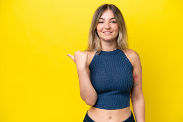 Wall Mural - Young Rumanian woman isolated on yellow background pointing to the side to present a product