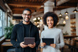 Portrait of happy entrepreneurs of caucasian and african american nationality standing next to each other and smiling at camera, Positive attractive business partners holding modern gadgets in hands