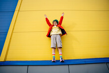 Boy With Arms Raised Standing In Front Of Yellow Wall