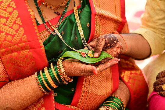 hands holding golden mangalsutra on leaf. Wedding indian jewelery. Bride and groom hands in mangalsutra ceremony. Henna hands. Wedding saree. Indian wedding rituals. Maharashtra wedding