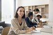 Happy mature Latin businesswoman, project manager, female team leader portrait. Positive business woman smiling at camera while with multiethnic colleagues working at laptop in background