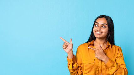 Indian millennial woman in casual excitedly pointing aside, blue background