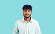 © Studio Romantic - Studio shot of a young Indian man with curly black hair. Portrait of an ethnic male model in a white shirt standing on a blue background and looking at the camera