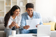 © Prostock-studio - Young Indian couple reviewing document, with laptop and coffee