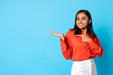 Happy arabic woman pointing at copy space over blue background