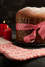 A Beautifully Presented Panettone Bread Wrapped With A Striped Red Ribbon, Accompanied By A Decorative Fabric With Festive Patterns, Set Amidst Ambient Candlelight.