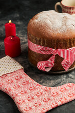 Panettone, The Classic Italian Treat, Sits Beautifully Next To Glowing Red Candles And A Festive Patterned Stocking, Capturing The Essence Of Christmas Celebrations