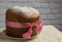 A Freshly Baked Panettone, Adorned With A Decorative Ribbon, Stands Against A Rustic Brick Background