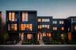 Modern black townhouses with illuminations inside, surrounded by vegetation at sunset.