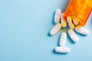 Wall Mural - White pills in orange bottle on blue background close up with copy space