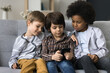 © fizkes - Three kids using smartphone together sitting on sofa, spend free time at home have fun with device, play cool new on-line games, friendly brothers watch funny videos in social network, browse internet
