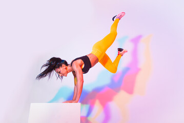 Wall Mural - Sportive beautiful woman training with athletic body and sportswear doing workout, colorful lighting and background