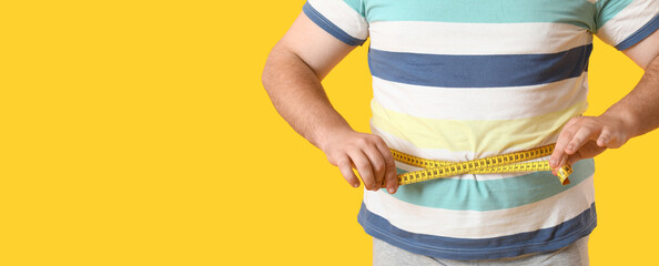 Overweight man measuring waist on yellow background with space for text, closeup