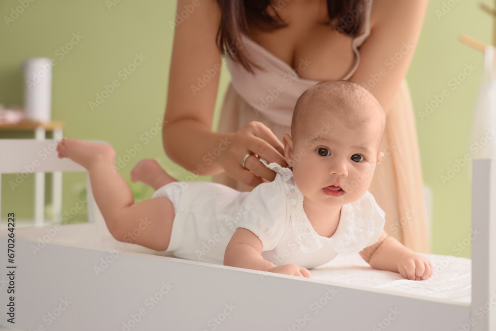 Mother dressing her cute little baby on changing table at home