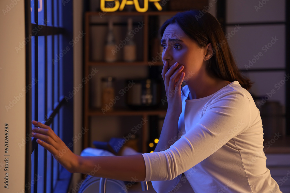 Beautiful young afraid woman in evening near window at kitchen