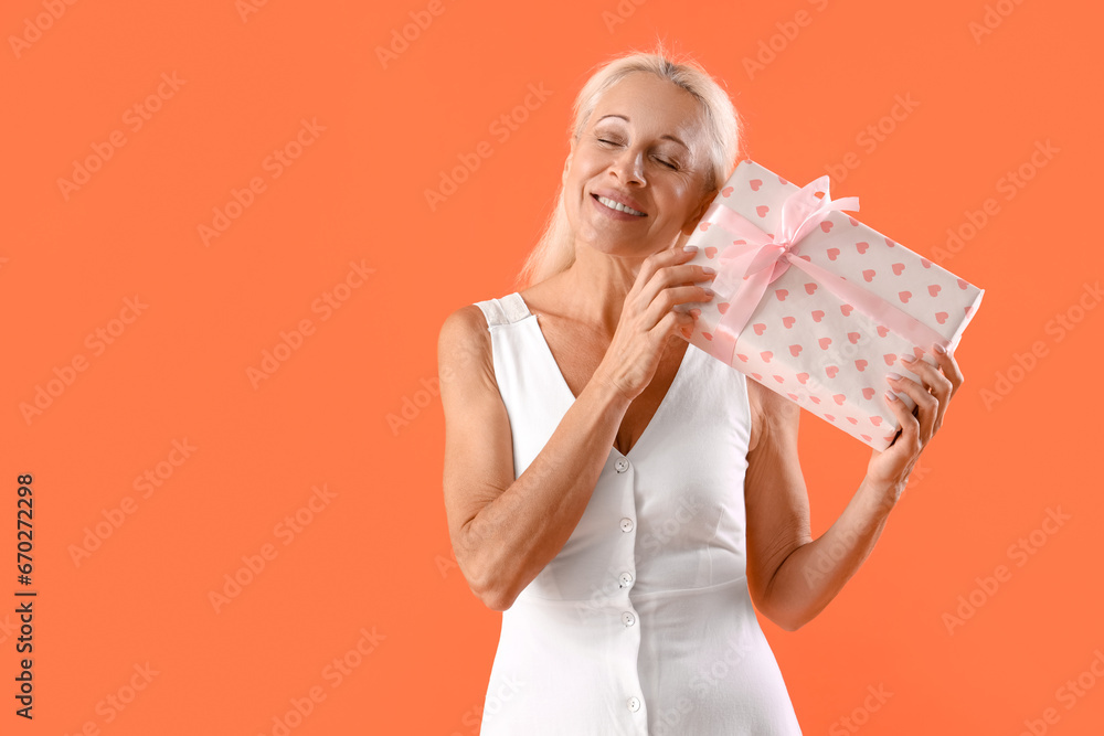 Happy mature woman with gift box on orange background