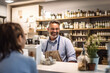 © JKLoma - a store clerk at the counter talking to a customer, smiling, happy, worker.
