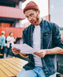 Pensive young man dressed in casual wear holding paper course work