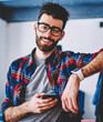 Cheerful hipster guy with cellular smiling at camera