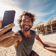 © pangamedia - An adult latin man is is making a selfie while smiling with with a telephone on a beach with a surfboard a high tech social media man