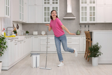 Poster - Enjoying cleaning. Happy woman in headphones dancing with mop in kitchen