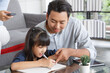 © aekkorn - Children education and home school concept : Young asisn father pleased to see little daughters' study success. Excited smiling small child girl enjoying learning and writing with pleasant dad at home