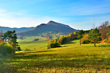 Fototapeta  - Autumn mountains landscape. Trees on a slope with dry grass and wooded mountains under blue sky with white clouds. View of Mountain Lackowa (997 msl) in Low Beskids. (Beskid Niski)