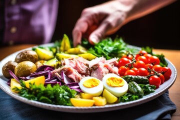 Wall Mural - a hand delicately placing a vegetable on nicoise salad