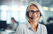 Happy old business woman in headset ready for online conference call, looking at camera. Mature female call center agent operator telemarketer talking consulting customer service support in office.