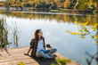 © olezzo - Young woman relaxing sitting on a wooden pier on a pond enjoying autumn nature