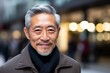 senior asian man with coat and scarf smiling at the camera