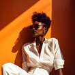 © CROCOTHERY - portrait of a cool and modern black woman with sunglasses in front of a orange wall background with copy space