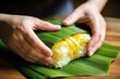 hand folding a banana leaf envelope filled with sticky rice and mango slices