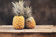 Eine reife Ananas in leuchtenden Gelb- und Brauntönen harmoniert mit dem sanften Grau des Hintergrunds, während lockere Pinselstriche die raue Textur unterstreichen