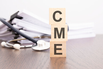 Poster - text CME is written on wooden cube near a stethoscope on a dark background.